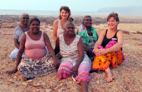 Indigenous women sitting on a beach smiling with members of the research team