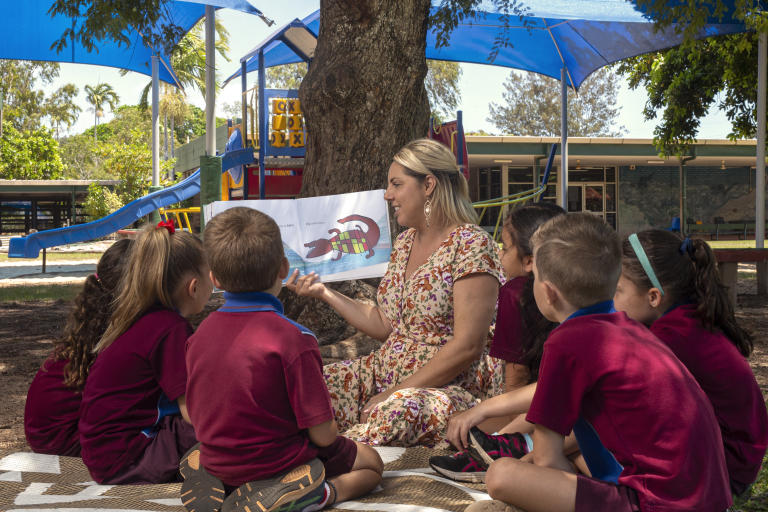 Alisha reading with children under a tree 