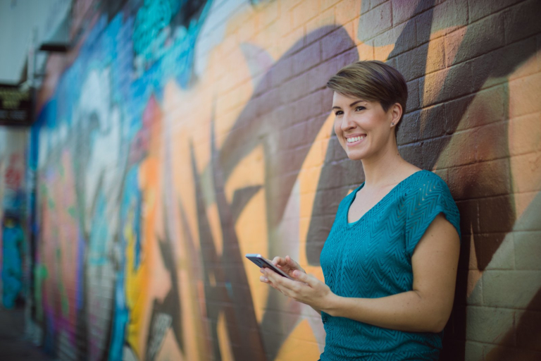 Student smiling with phone in hand with a graffiti background