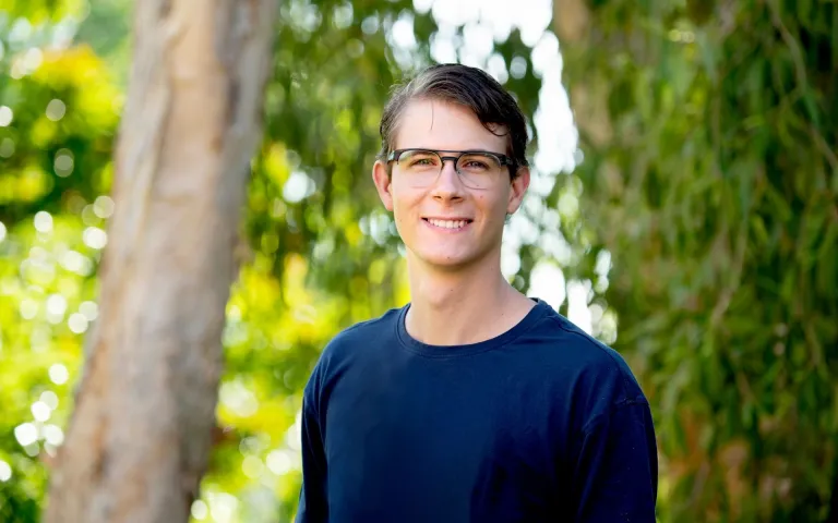 CDU student Drew Whitehouse smiling at the camera surrounded by trees