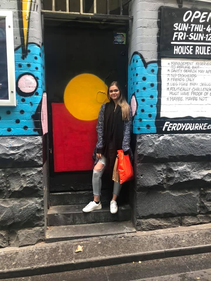 Shailee standing in front of a door painted with the Aboriginal flag