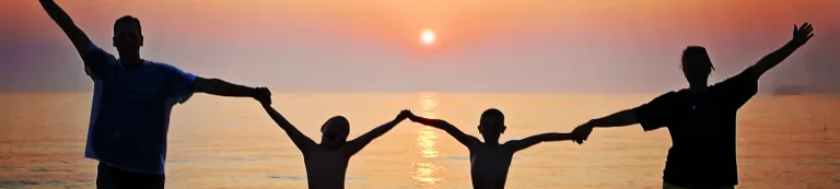 Family holding hands, silhouetted against the setting sun