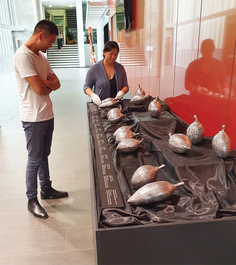 Eileen Lim installs cast metal boab nuts – part of the BOAB100, 2014 undertaken by artists from Waringarri Arts in the Colonnade, Chancellery, Casuarina campus, CDU while Phillip Du watches.