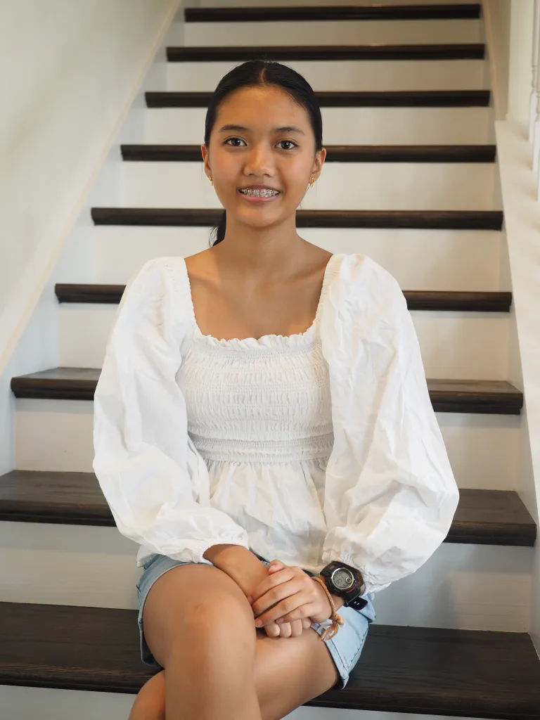 Woman sitting on stairs wearing white blouse with a smile