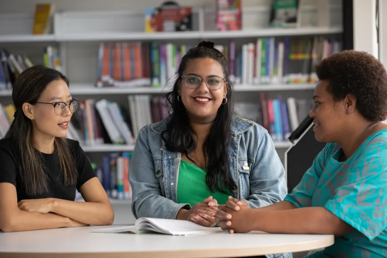 Three students discussing their studies in a library setting