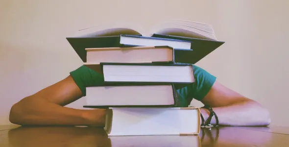 Student slouched behind a pile of books