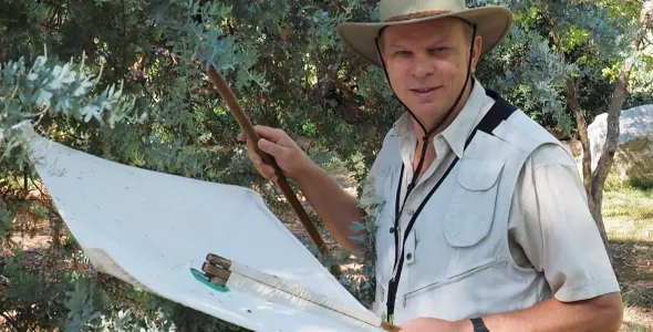 Rolf Oberprieler, wearing a hat, standing in front of a tree with a small white sheet and a stick