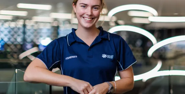 Eliza Kimlin from waist up, wearing blue shirt with NT fisheries logo, with out of focus lights in background