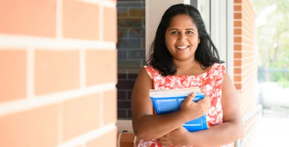 Indigenous Australian teacher holding books in regional school