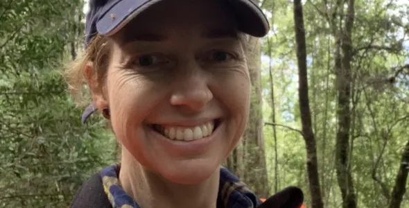 Anna Richards wearing CSIRO cap and high vis vest, with tall trees in background