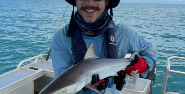Person wearing hat and sunglasses standing in a boat holding a small shark