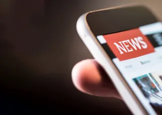 A smartphone being held with 'news' written on the screen