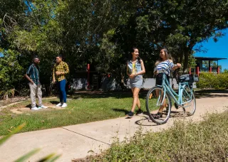Two female students walking their bikes and smiling