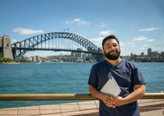 CDU nursing student in front of the Sydney Harbour Bridge holding a laptop