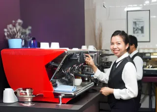 a woman smiling holding a cup near a coffee machine 