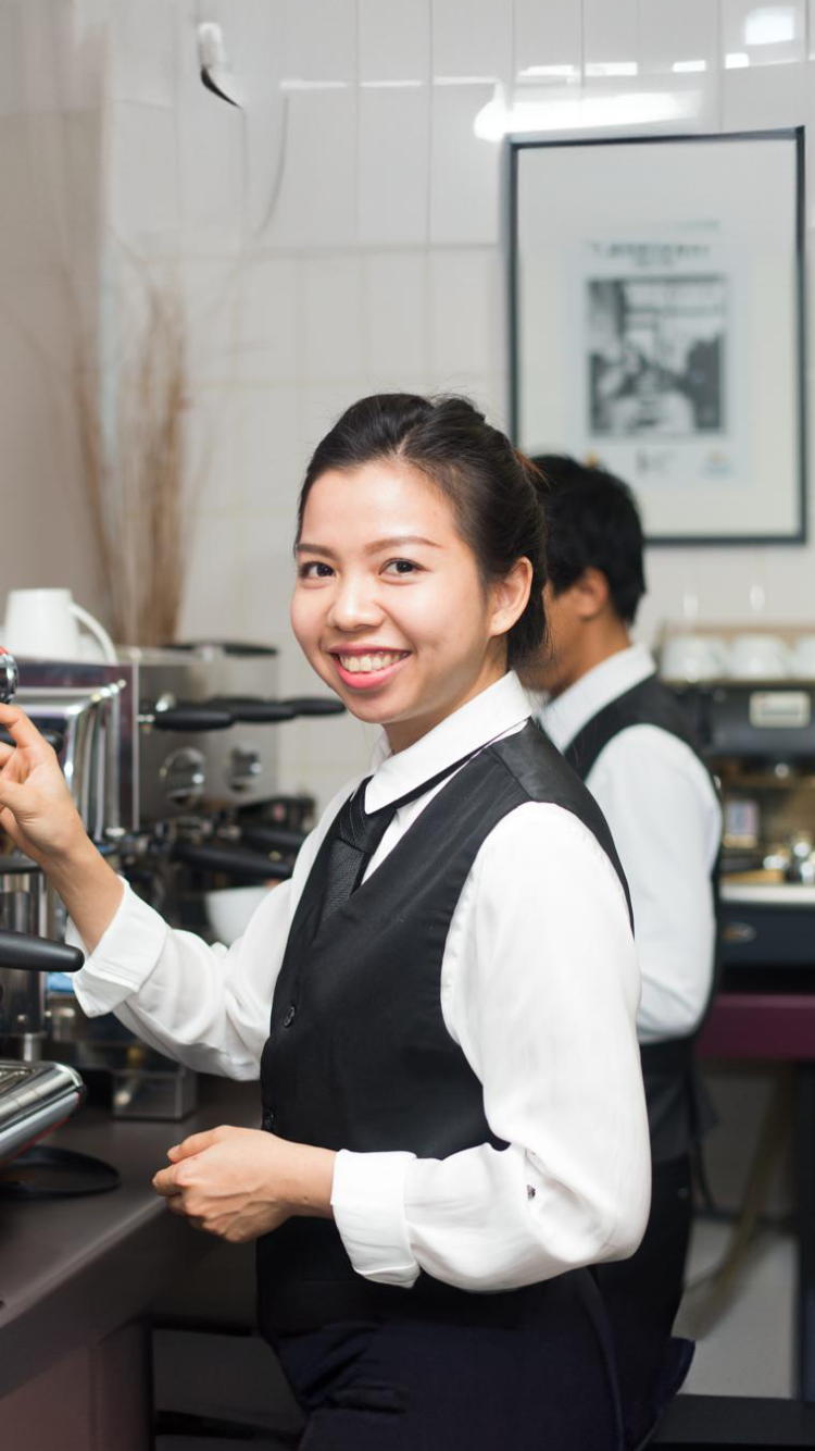a woman smiling holding a cup near a coffee machine 