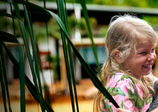 CDU graduate Jolene holds daughter smiling in front of pandanus tree