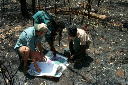 three people looking at maps on burnt ground