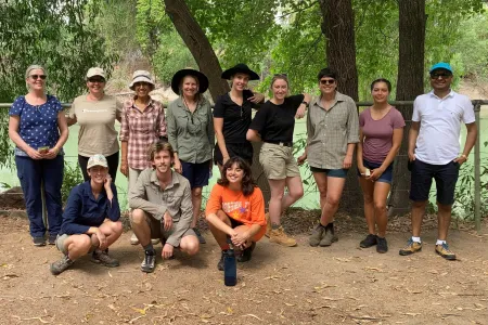 12 people posed in front of a fence with river in background