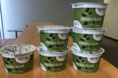 six plastic pots of Kakadu plum yogurt on a table, with bare white walls in the background