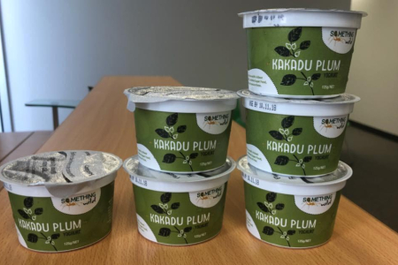 six plastic pots of Kakadu plum yogurt on a table, with bare white walls in the background