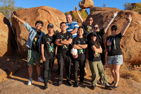 group of people wearing National Science Week tee-shirts posing in front of large rocks.