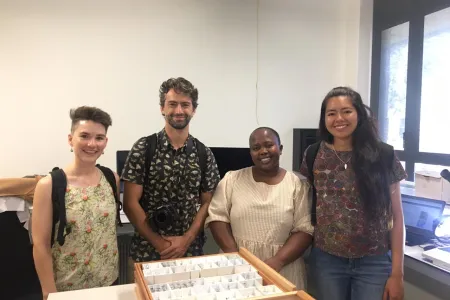 Four people standing in a row smiling, behind a display case with contents that are not visible