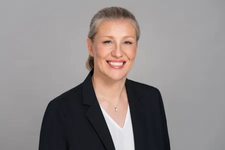 Woman with black jacket, blonde hair, blue eyes, smiling towards camera