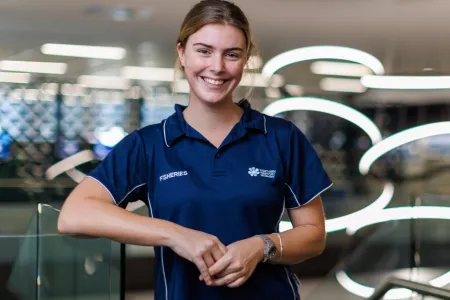 Eliza Kimlin from waist up, wearing blue shirt with NT fisheries logo, with out of focus lights in background