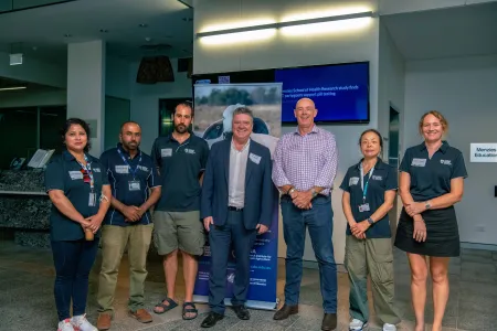 seven people standing in a curved row, posing for this photo, inside a building, with a vertical banner partly visible behind them.