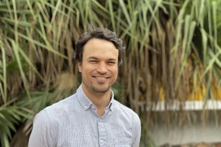 Dr Clement Duvert, head and shoulders, with green spiky-looking leaves hanging down in background