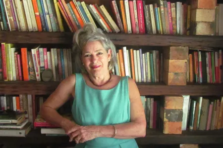 Female middle aged author stands in front of book shelf smiling with light aqua dress