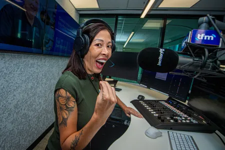 A woman stands in front of a mic in a radio studio. 