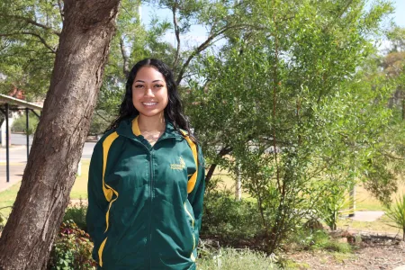 student stands outside in green and gold uniform