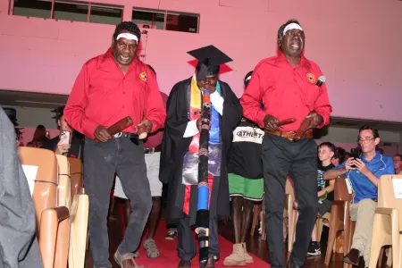 two TOs walk down read carpet with one graduate playing yidaki