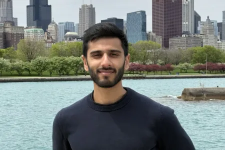 photo of a man standing and smiling with water and buildings in the background