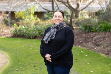 Photo of woman standing and smiling at camera with patch of grass in the back