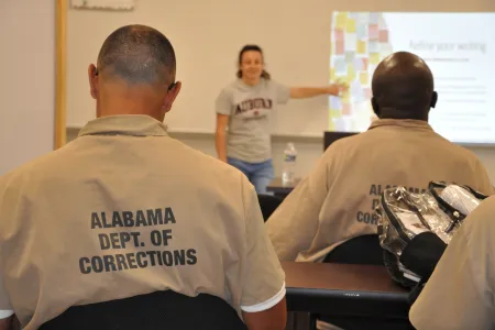 Men from corrections facility with back facing the camera, woman in the back standing and point at slides