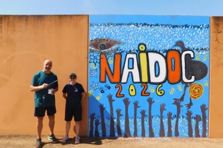 Charles Darwin University lecturers and Ywrite workshop facilitators Dean Mobbs and Adelle Sefton-Rowston next to a 2026 NAIDOC mural. Picture: Darwin Correctional Precinct