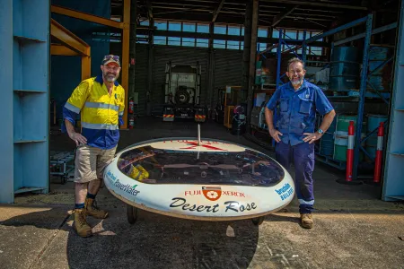 two males stand on either side of solar car