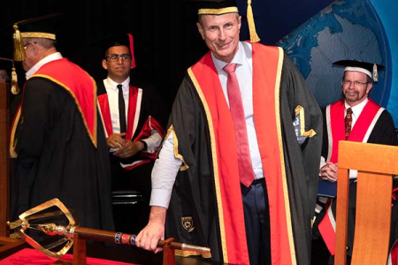 The Hon Paul Henderson AO, with his hand on the university mace, formally takes on the role of Chancellor of Charles Darwin University.