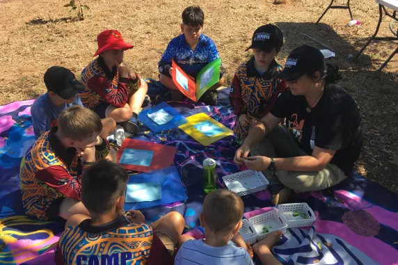 Children and Carla sitting on cloth on ground doing science
