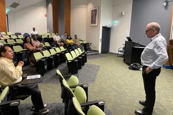 People sitting in lecture room with one person standing in front talking to them