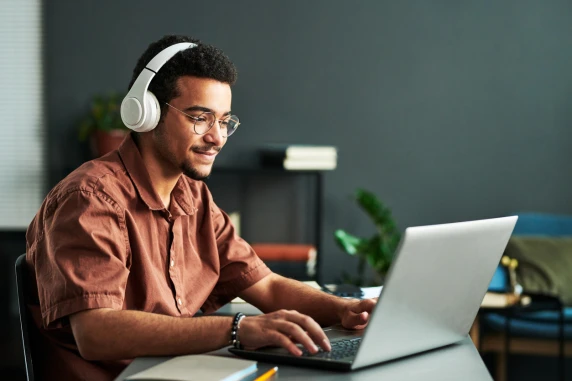 Male student with headphones looking at a laptop