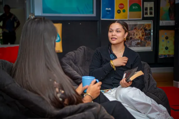 Two students seated down with one students back facing the front