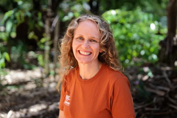 woman with ochre shirt smiling with blonde curly hair