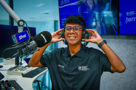 A Territory FM presenter smiles at the camera inside CDU's radio studio