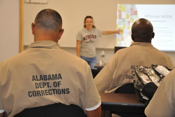 Men from corrections facility with back facing the camera, woman in the back standing and point at slides