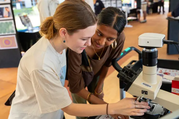 2 students looking at some reference images in front of a microscope