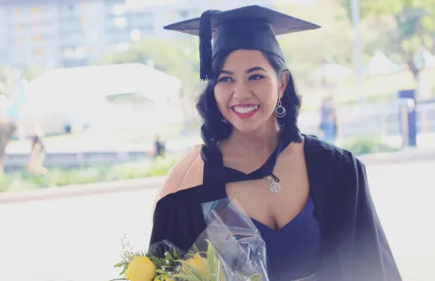 CDU student Enggar Daranindra in a graduation gown and cap smiling at the camera
